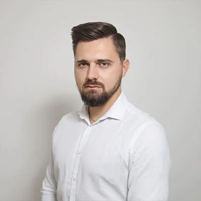 A man with a beard wearing a white shirt poses against a plain background.