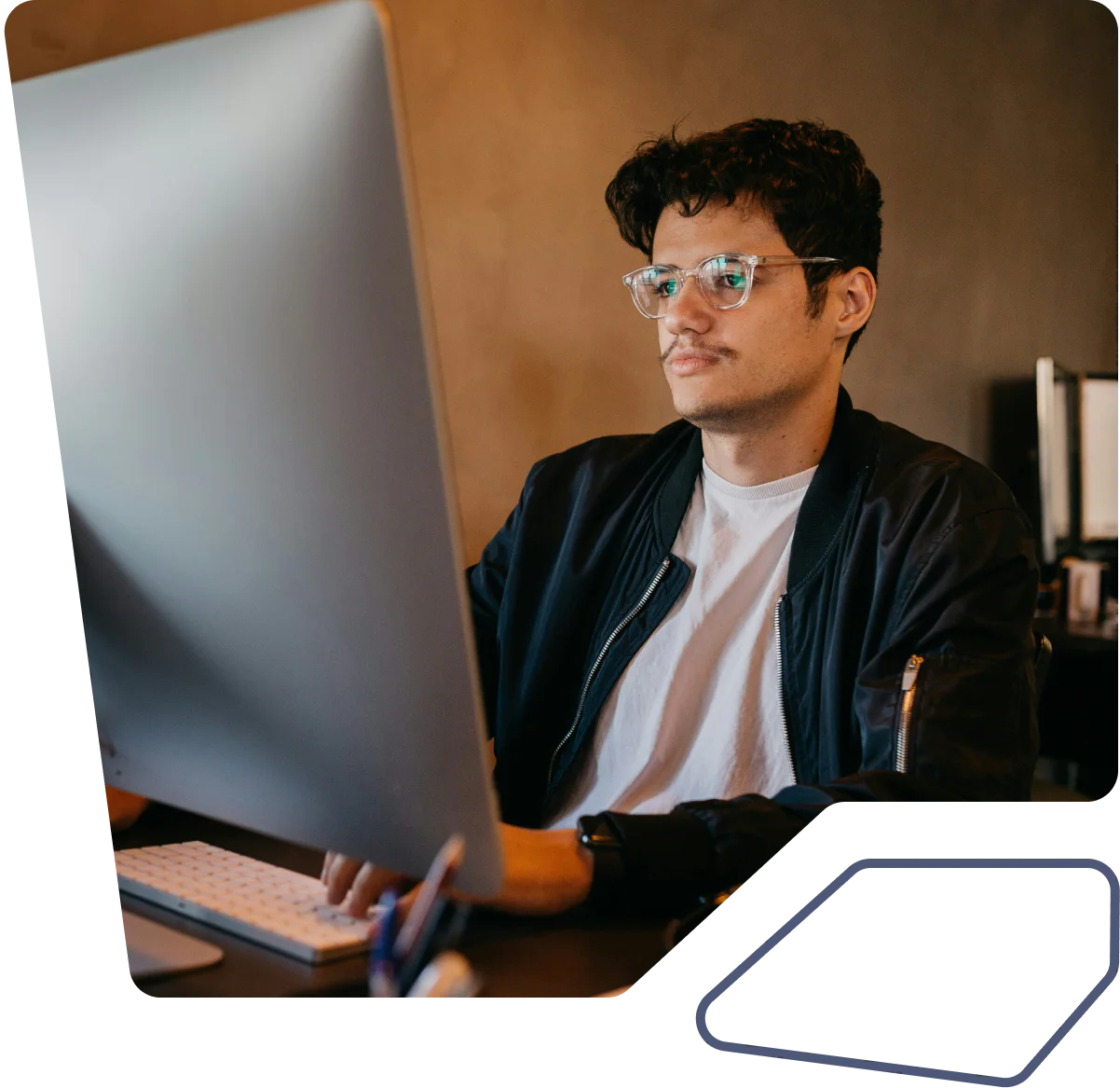 Man with glasses working on a desktop computer at a desk.