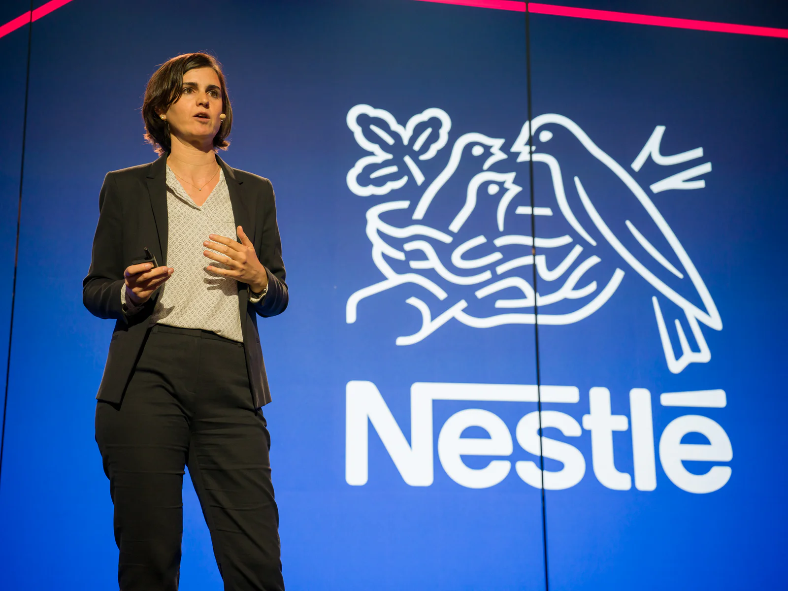 Woman presenting on stage with Nestlé logo in the background.