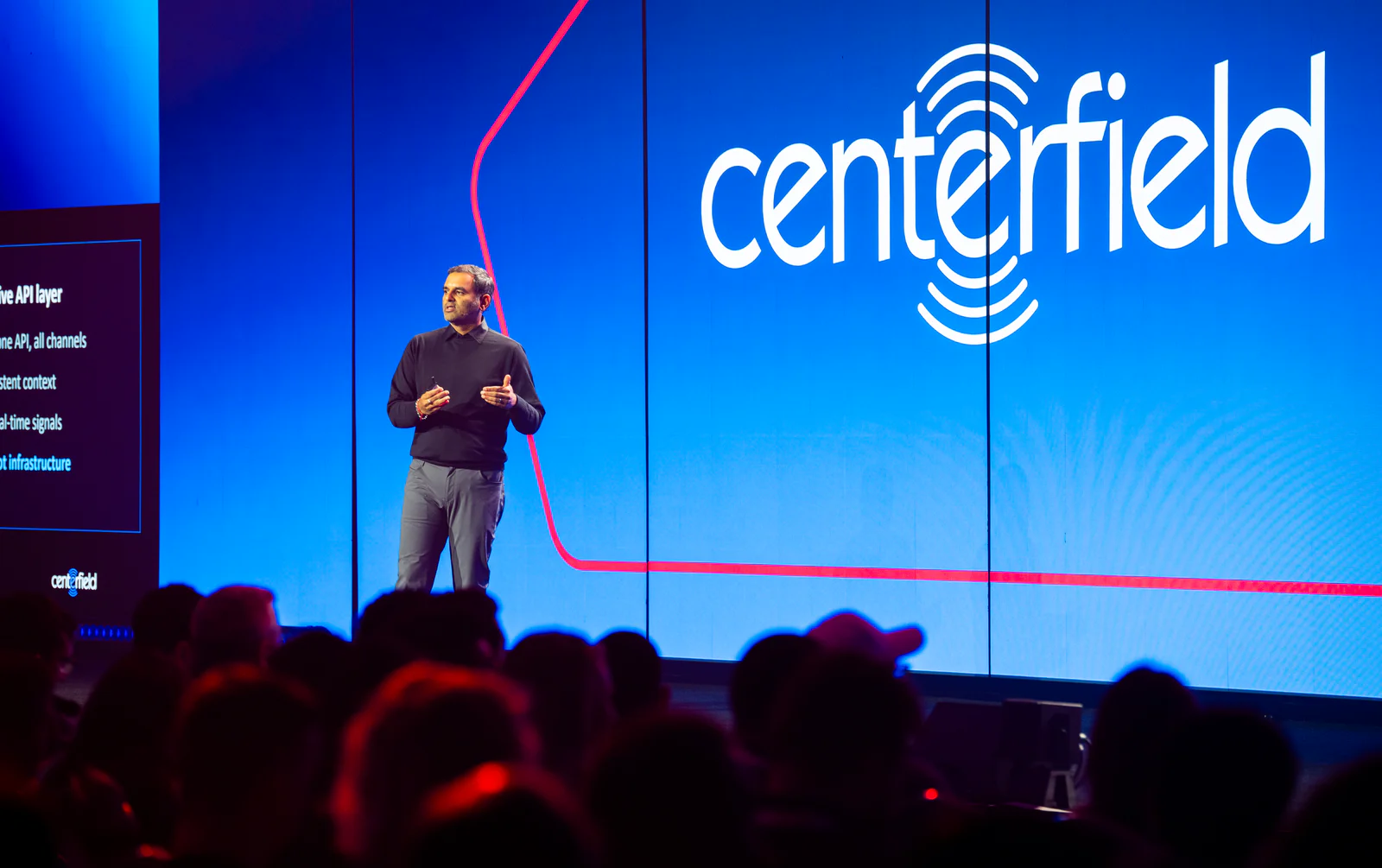 A speaker on stage presenting at the Centerfield conference with a large blue screen behind him.