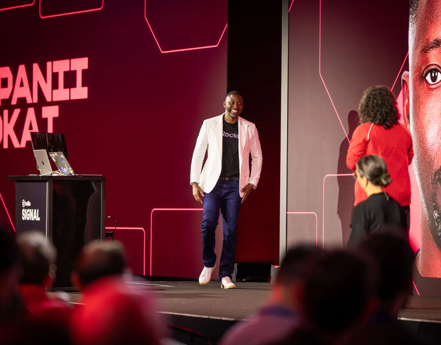 Man smiling as he walks onto the stage during a technology conference.
