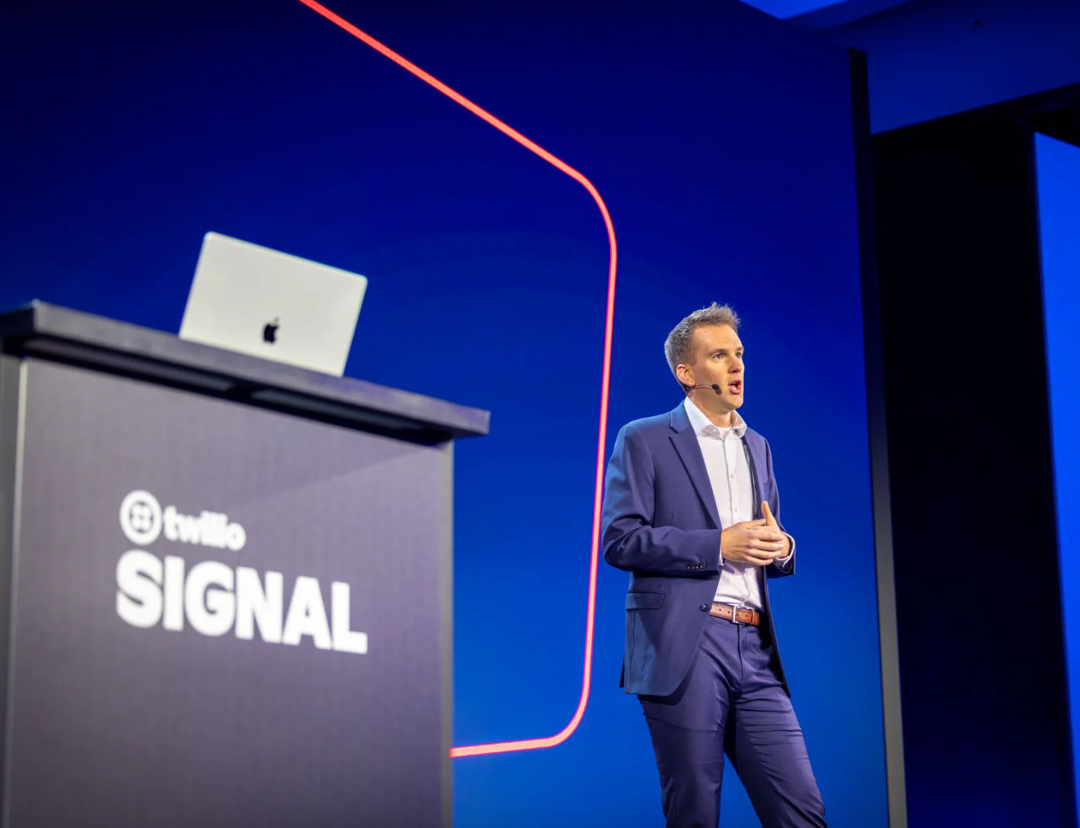 Man in blue suit speaking on stage at Twilio Signal conference with presentation screen and podium.