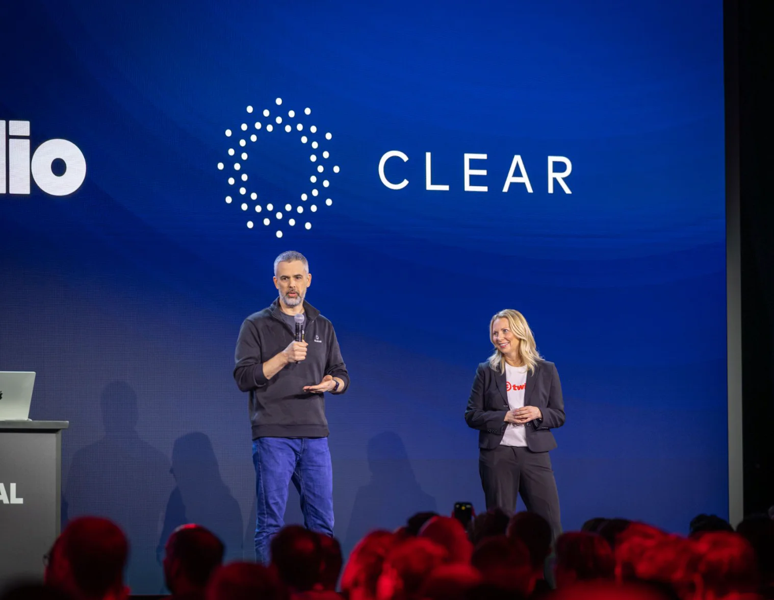 Two speakers on stage at a technology conference with a logo displaying the word CLEAR.