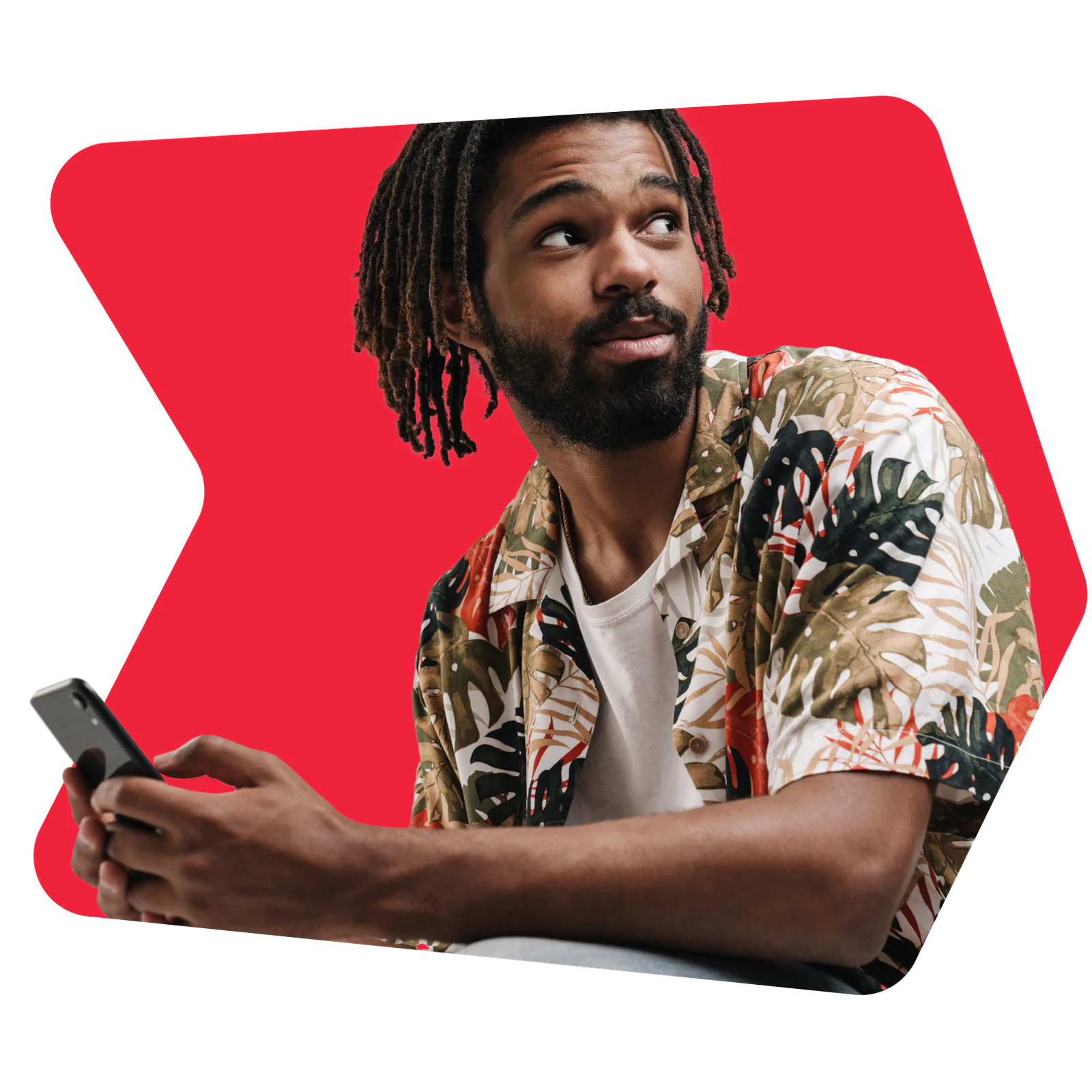 Man with dreadlocks looking over his shoulder while holding a smartphone. Man with dreadlocks in a tropical shirt holding a smartphone in front of a red background.