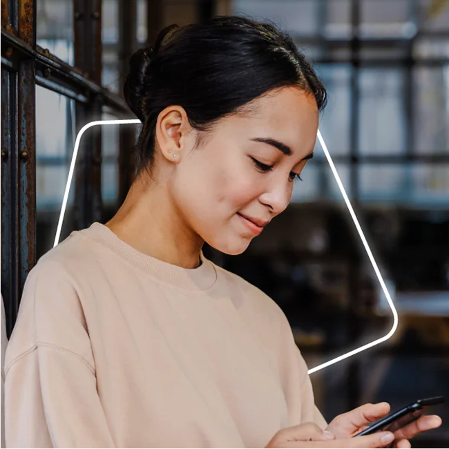 Woman in a beige sweater looking down at a smartphone