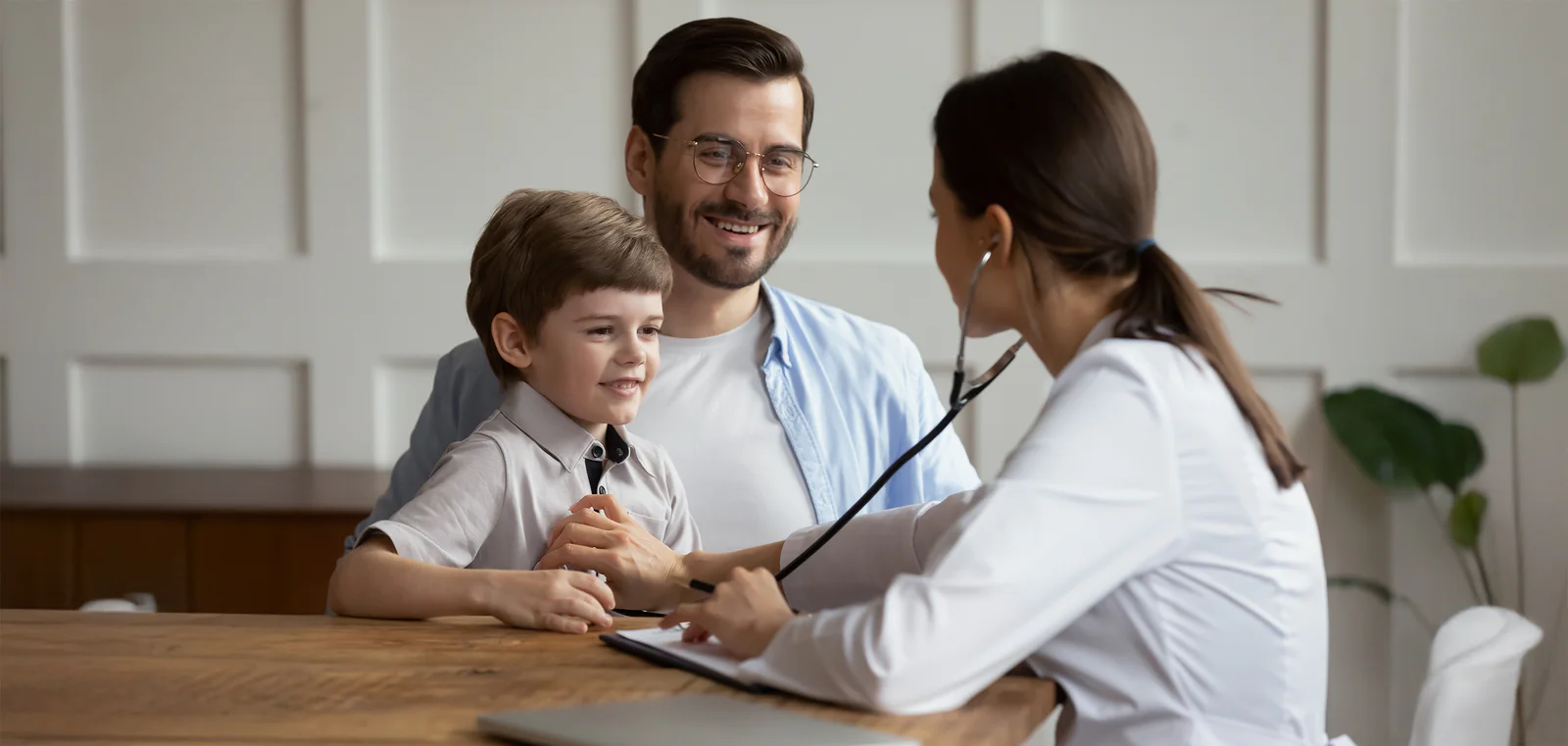 Doctor Examining Smiling Child with Parent Doctor using stethoscope to check a smiling child while the parent looks on.
