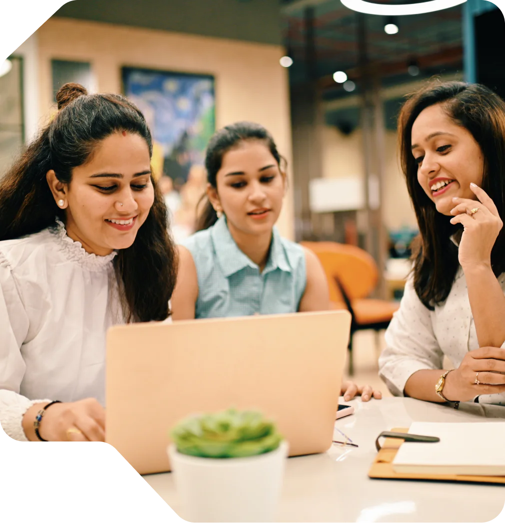 Three women working together at a laptop in an office environment.