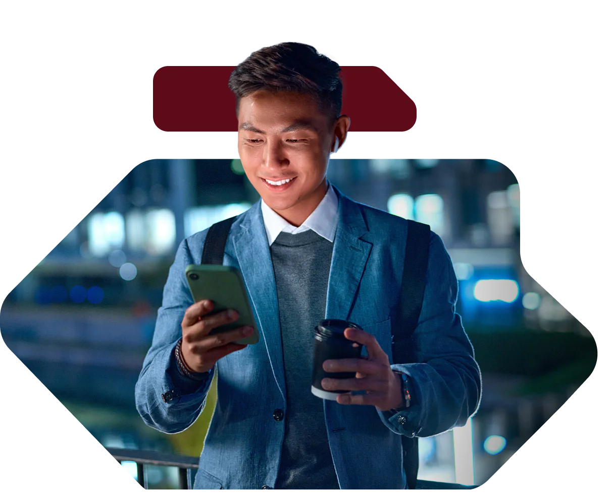 Young man in a suit jacket holding a smartphone and a coffee cup, standing outdoors at night