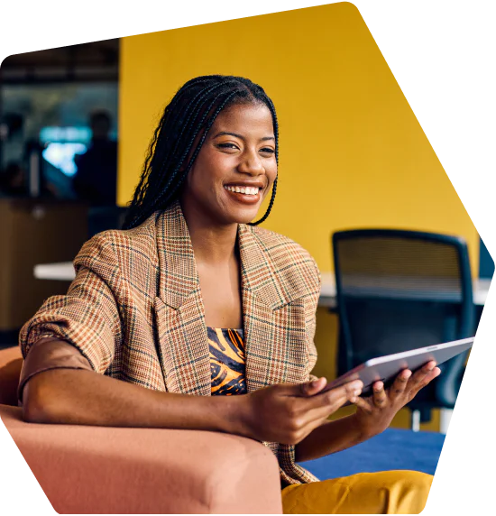 Woman in a plaid blazer sitting and smiling with a tablet in her hands