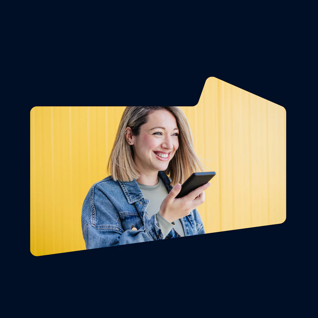 Woman smiles while pointing a smartphone, standing in front of a yellow background