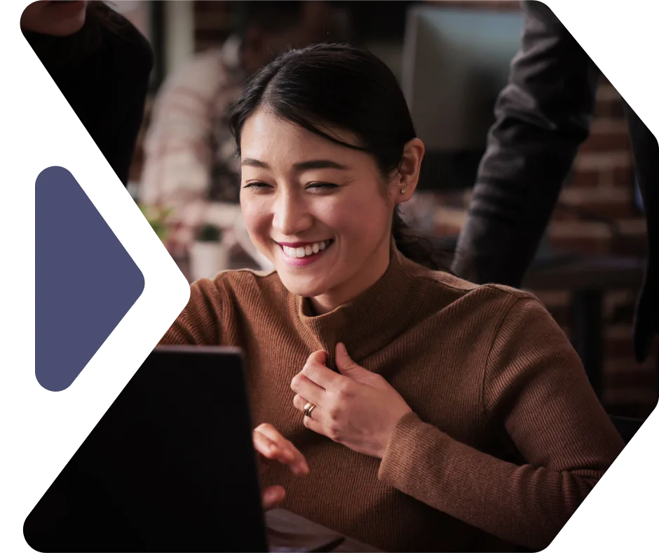 Woman smiling while using a laptop in an office environment.