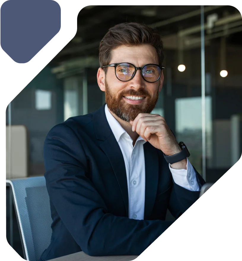 A man in a suit wearing glasses smiles while sitting in a modern office.