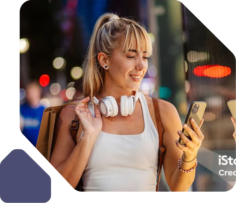 Woman Using Smartphone on a City Street at Night Smiling woman with headphones looking at her smartphone while standing on a city street at night.