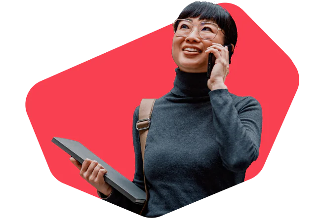 Woman with glasses talking on phone while holding a tablet, wearing a dark turtleneck and bag.