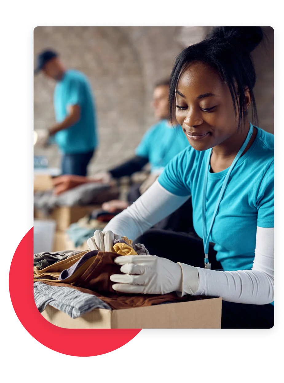 Woman wearing gloves organizing clothes at a volunteer event with other people in the background.
