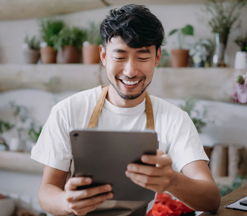 Man with an apron smiling while looking at a tablet in a plant shop.