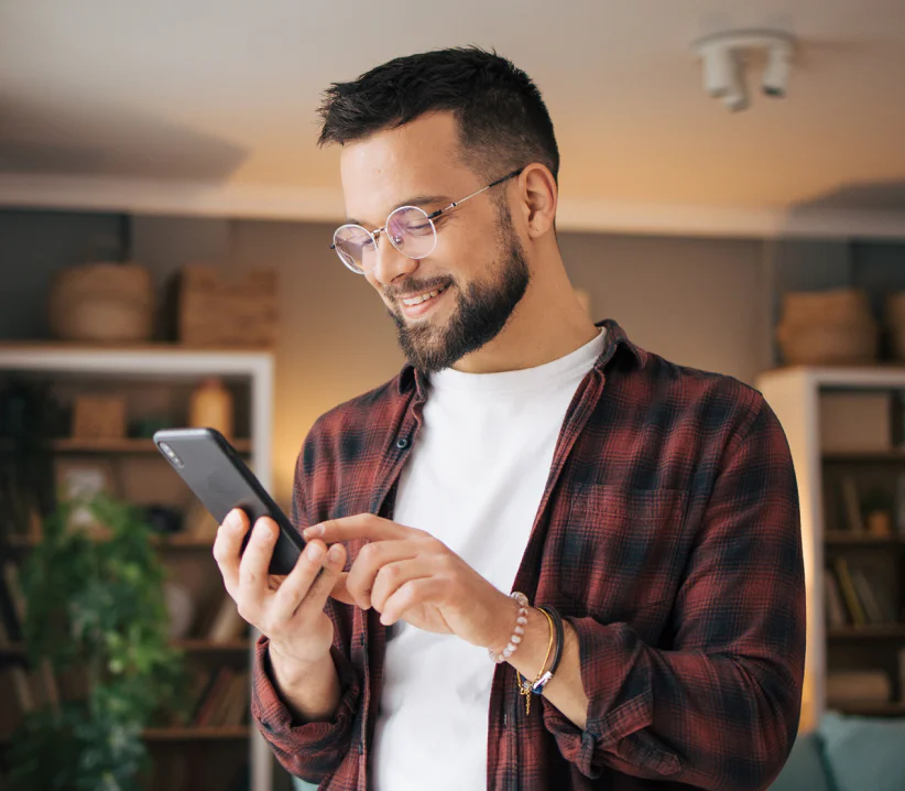 Man with glasses checking his phone in a cozy room.