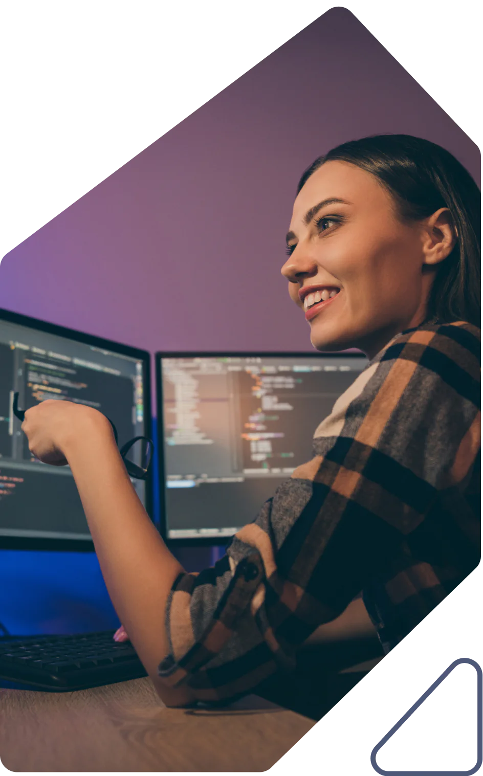 Smiling woman coding on dual monitors with a purple backdrop