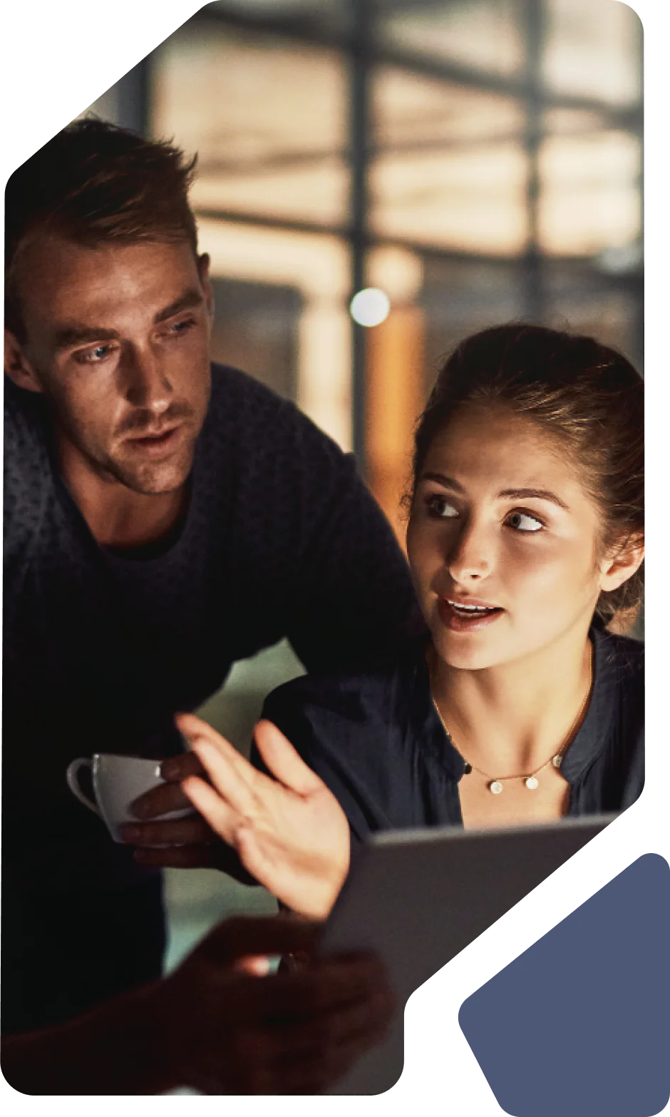 Two colleagues engaged in discussion over a tablet in a modern office environment.