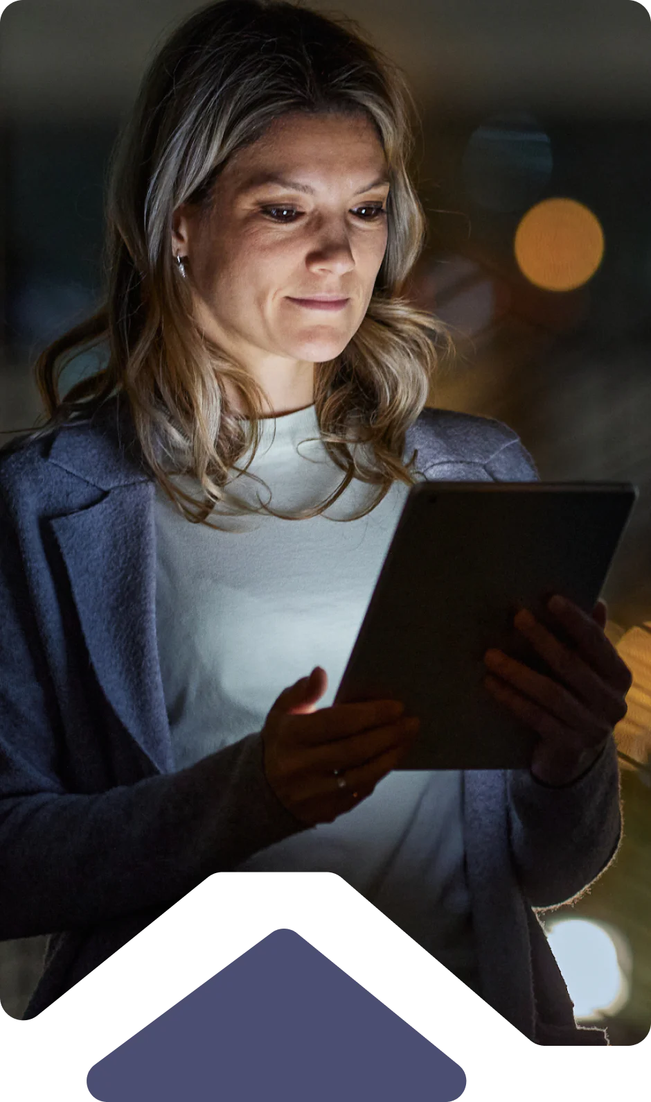 Woman holding and looking at a tablet screen in a dimly lit environment.