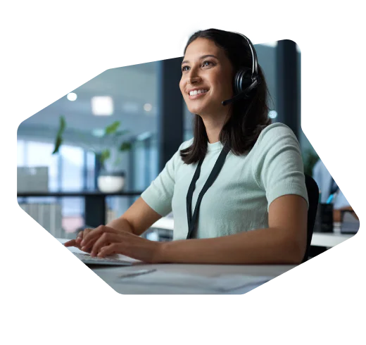 Woman smiling, wearing a headset while working on a computer at a desk in an office setting.