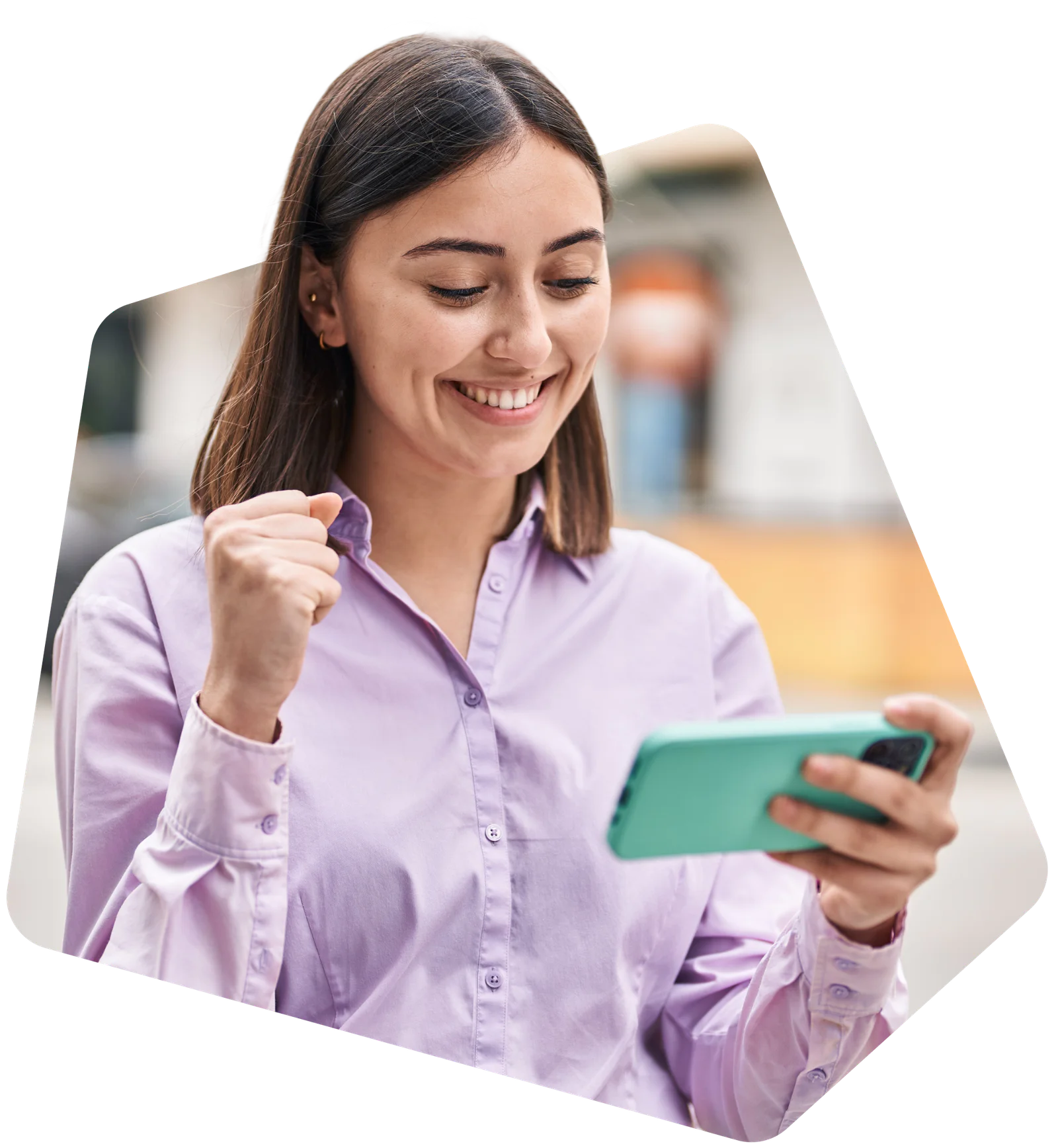 Woman in a light purple shirt holds her phone and makes a fist as she looks at the screen with a smile.