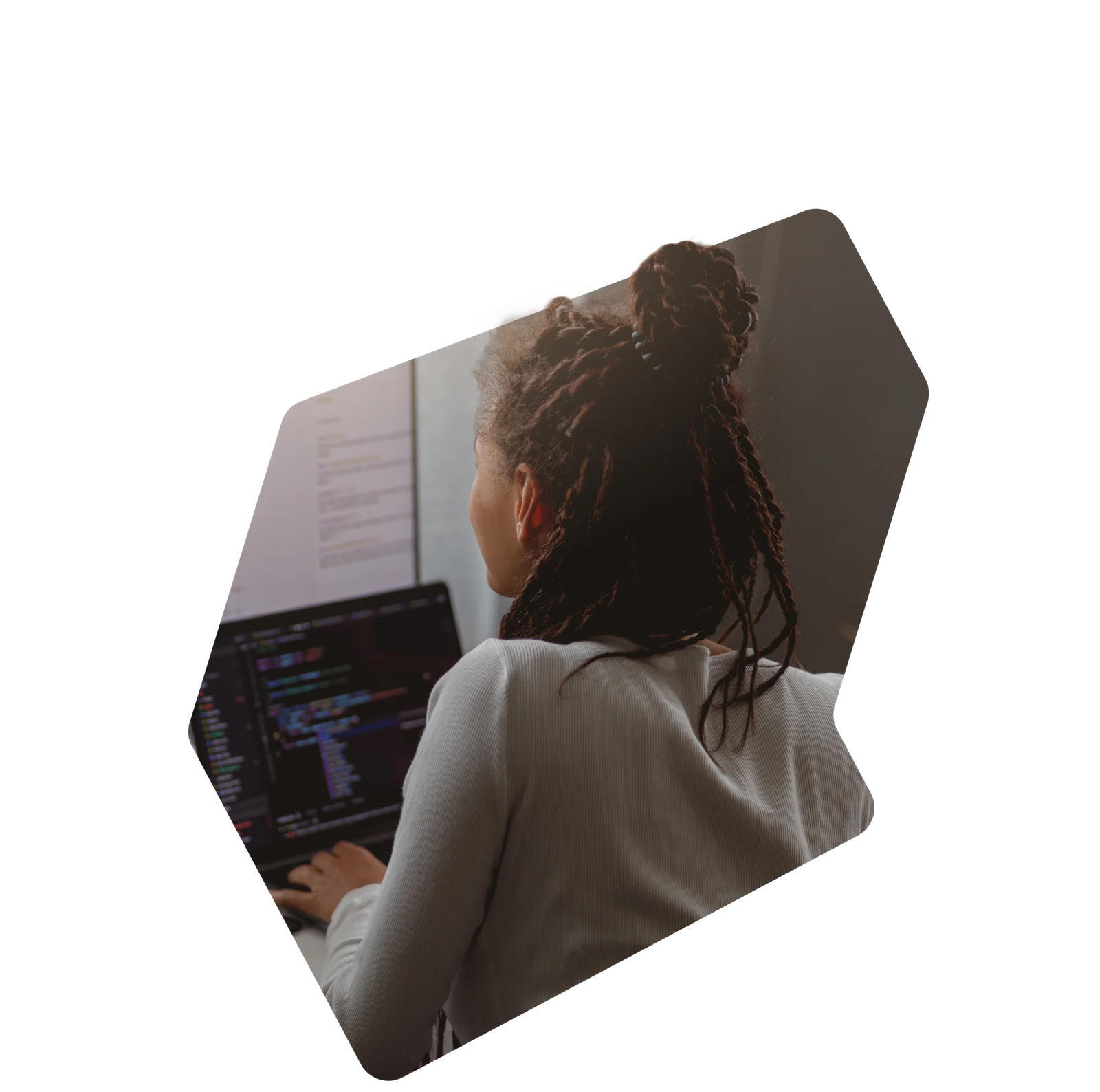 Person with dreadlocks typing on a laptop with code on the screen
