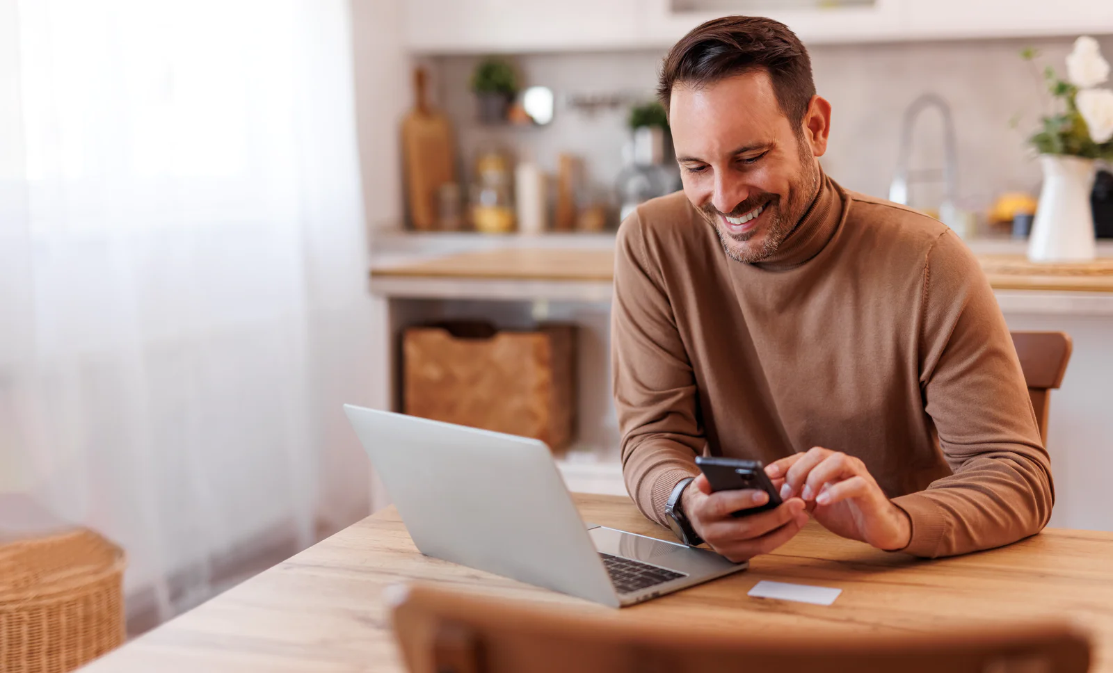 Portrait of smiling mid adult man with credit card using mobile phone and laptop on dining table at home