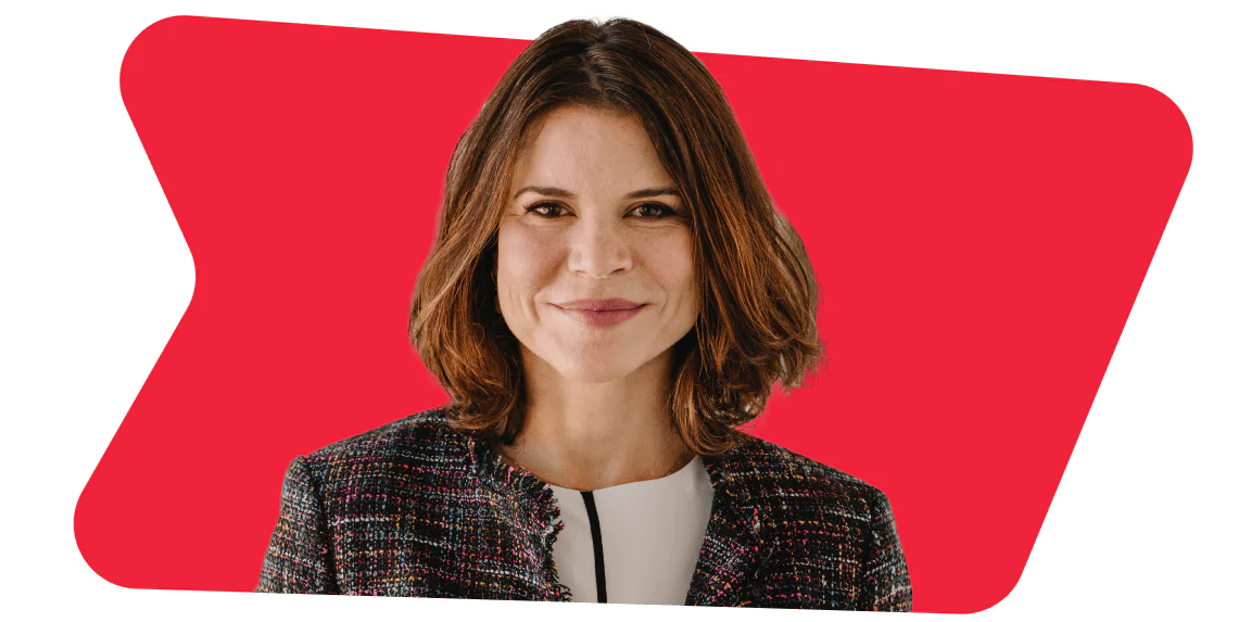 Woman with shoulder-length brown hair, wearing a business suit, standing against a red background.