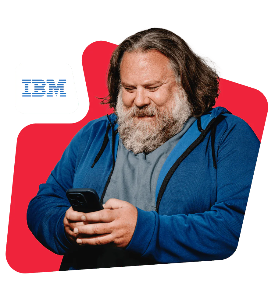 Man with beard in blue hoodie looking at a smartphone with IBM logo nearby.