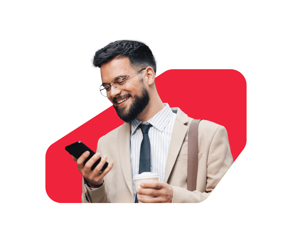 A smiling man in a suit looks at his smartphone while holding a coffee cup.