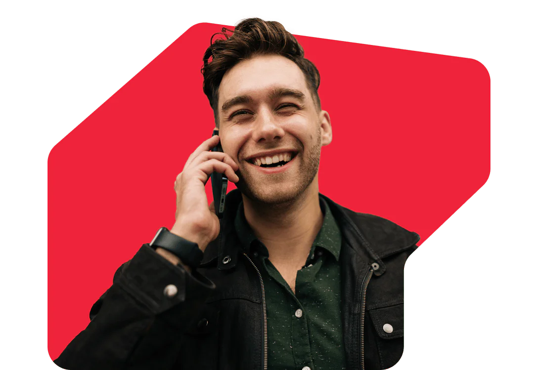 Smiling Man Talking on the Phone A smiling man holding a phone to his ear, wearing a dark jacket and green shirt with a red background.