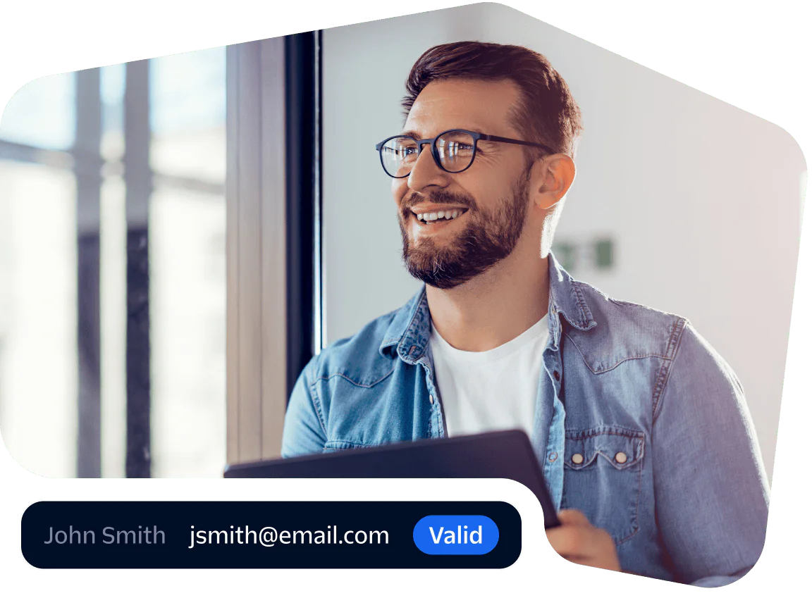 Smiling professional verifying email with a tablet Man in glasses and denim shirt smiling while using a tablet near a window.