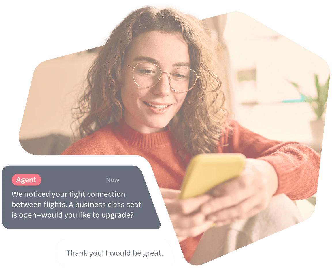 Woman smiles while reading a phone, screen shows a chat offering a business class seat upgrade.