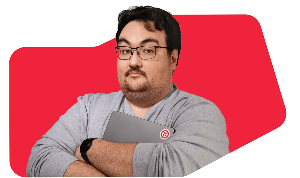 Man wearing glasses and a gray shirt, holding a laptop in a red background