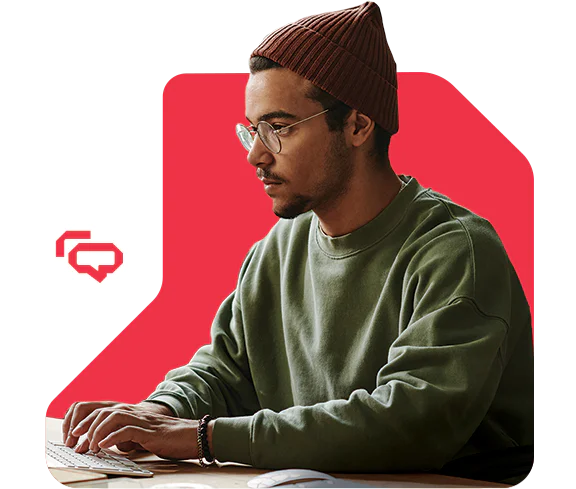 Man wearing glasses and a beanie types on a keyboard against a red background.