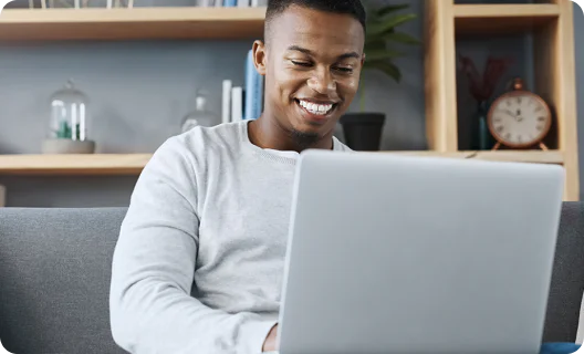 Man sitting on a couch and smiling at a laptop screen with bookshelves in the background.