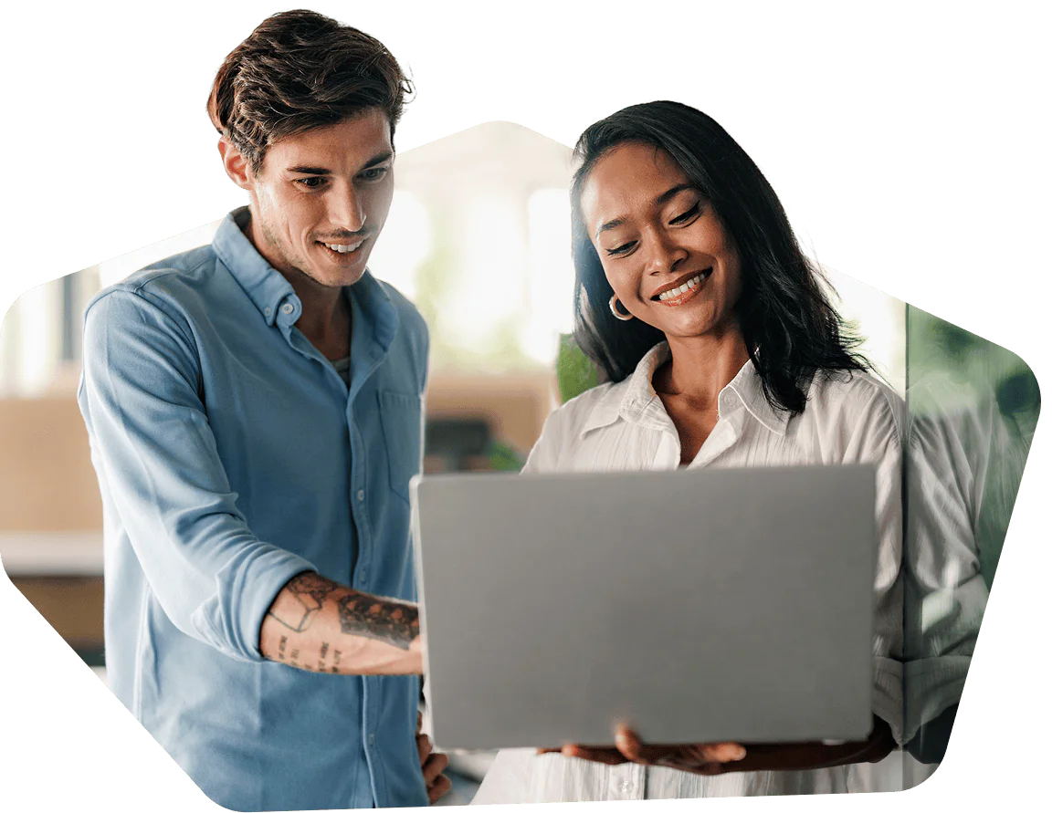 Two colleagues smiling and working together on a laptop in an office setting.