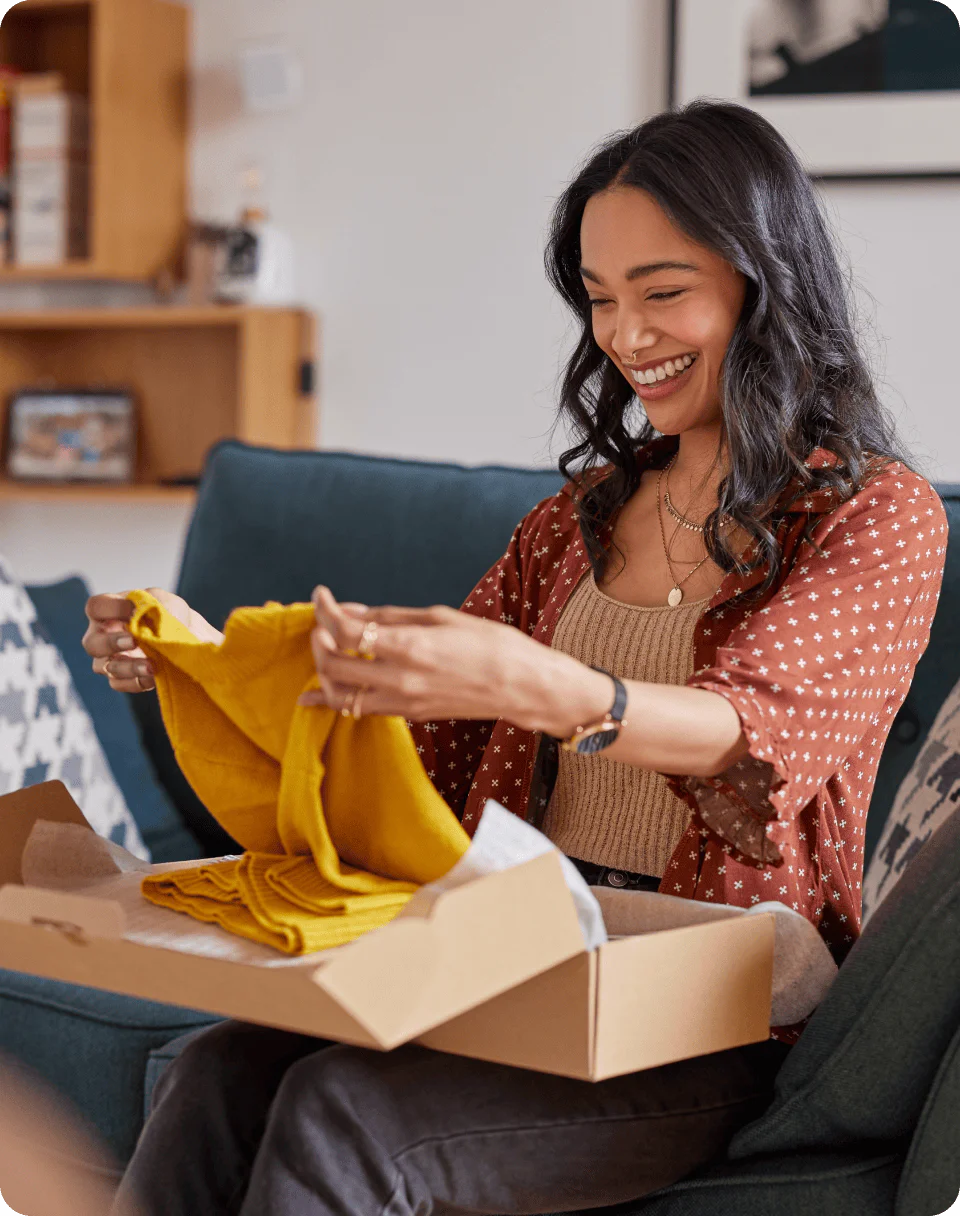 Woman smiling while holding a yellow sweater from an open cardboard box