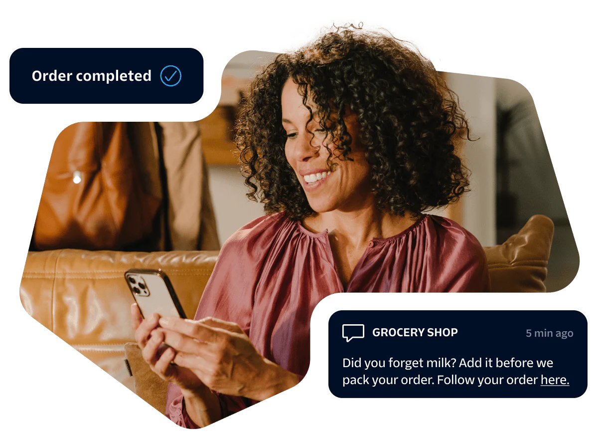 Woman smiling at her smartphone while receiving an online grocery order confirmation message.