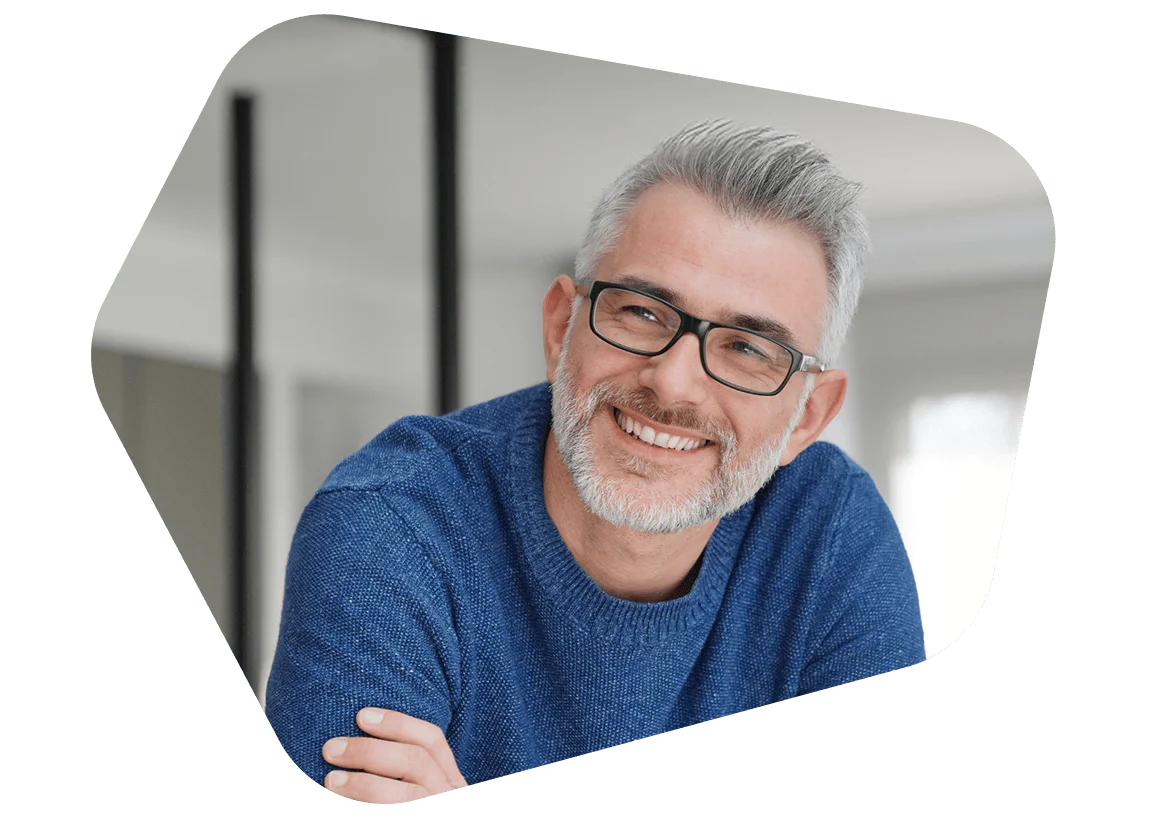 Man with grey hair and glasses wearing a blue sweater smiling indoors