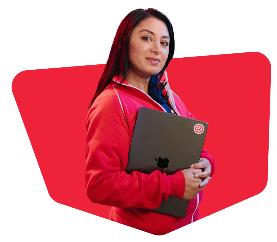 Woman in red jacket holding a laptop against a red background, looking confidently at the camera.