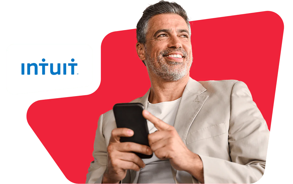 Man Using Smartphone in Front of Intuit Logo Smiling man holding a smartphone with Intuit logo in the background.