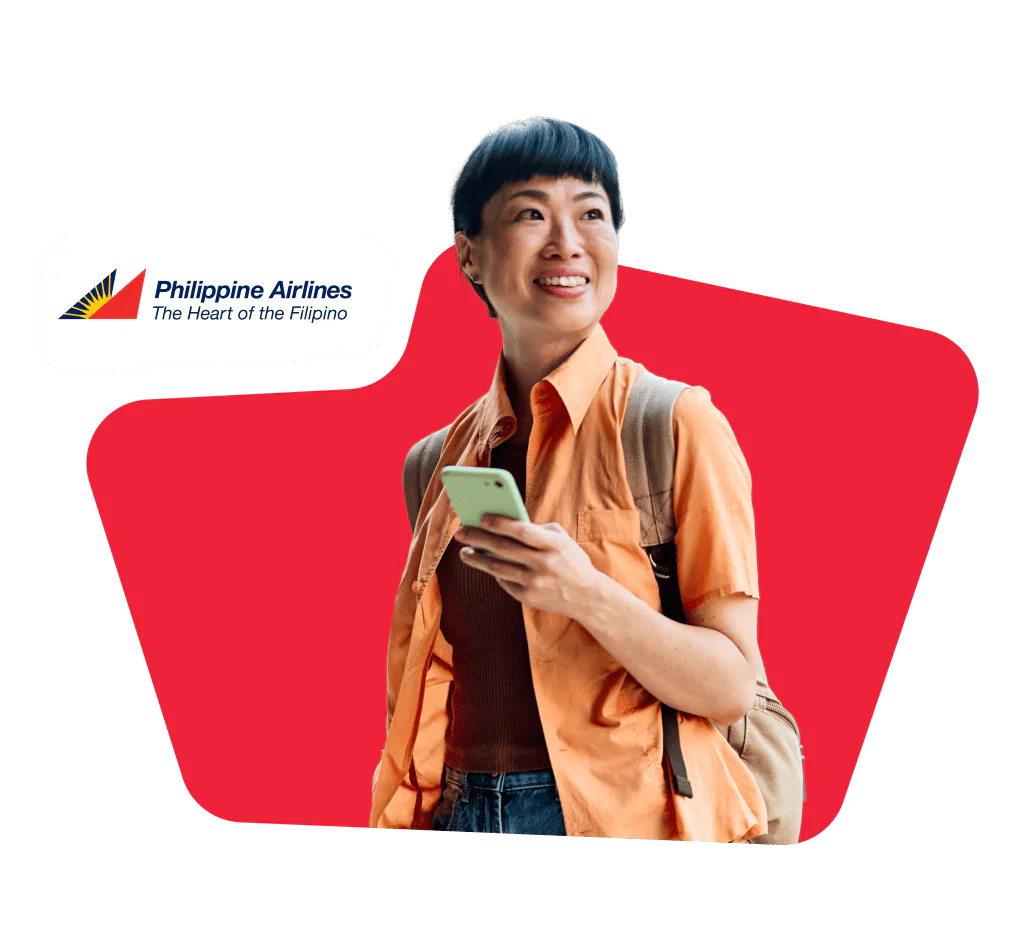 Smiling woman in an orange shirt holding a phone with a Philippine Airlines logo in the corner