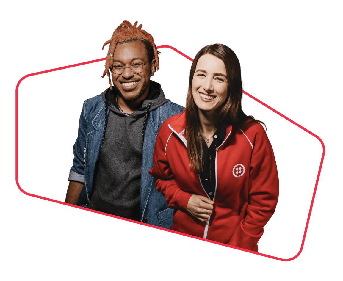 Two people, one in a red jacket and the other in a denim jacket, smiling against a transparent background.