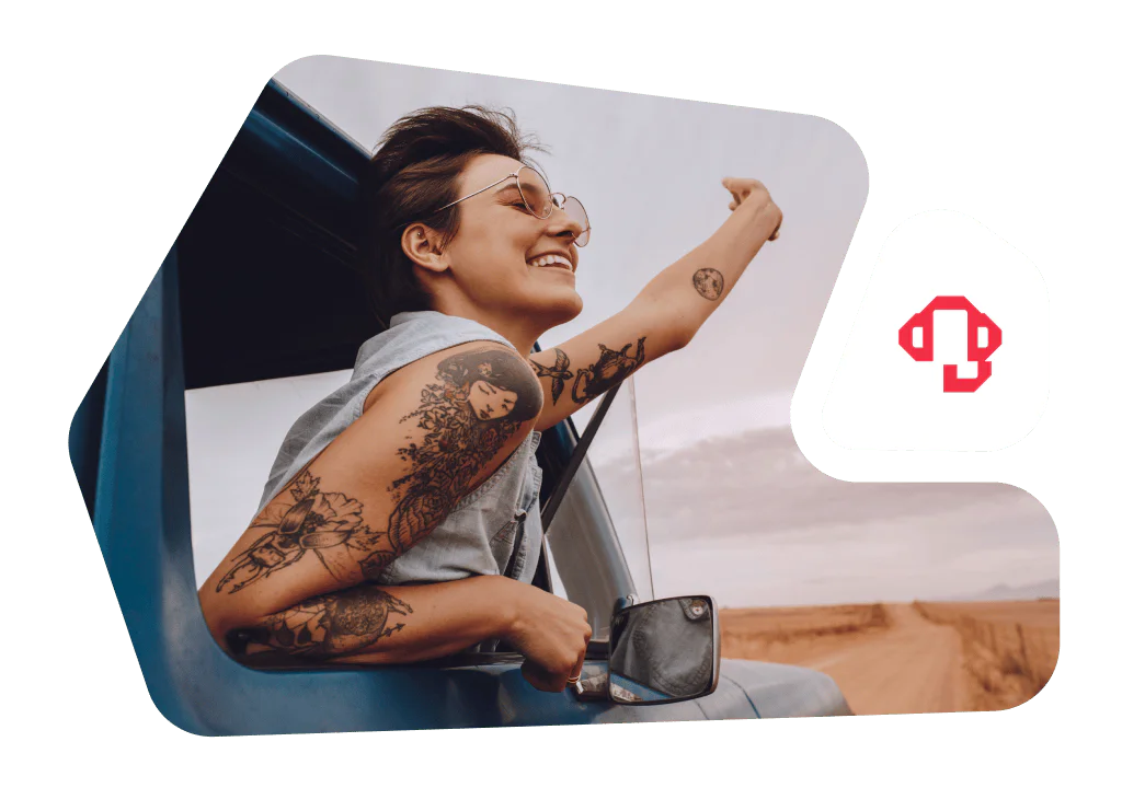 Woman with tattoos smiling and sticking her arm out a car window during a road trip