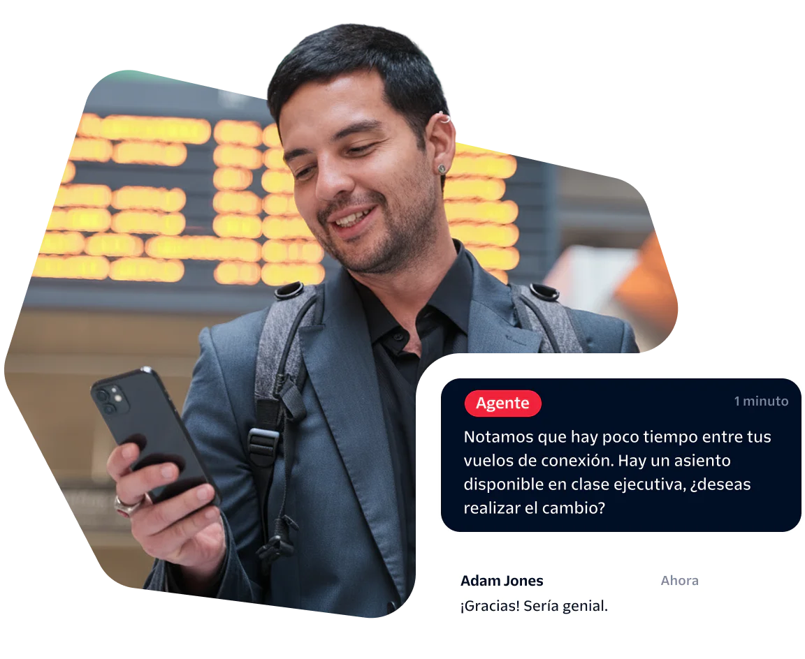 Man checks phone at airport, receives message about upgrading to business class, smiles.