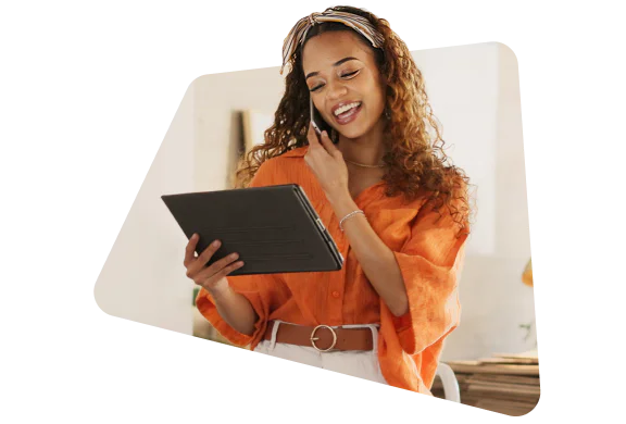 Smiling woman in an orange shirt using a tablet and talking on the phone.
