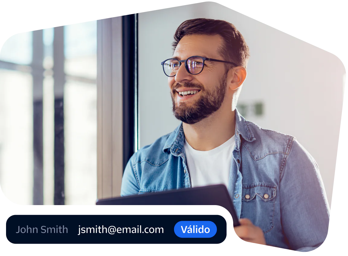 Smiling professional verifying email with a tablet Man in glasses and denim shirt smiling while using a tablet near a window.