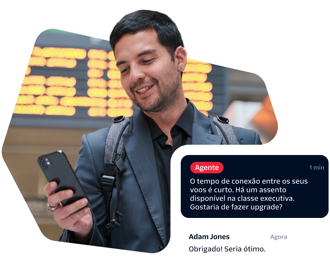 Man checks phone at airport, receives message about upgrading to business class, smiles.